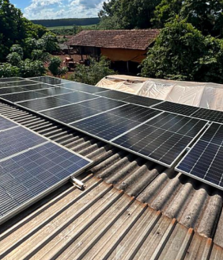 Painéis solares instalados em propriedade rural, com casa e mata ao fundo