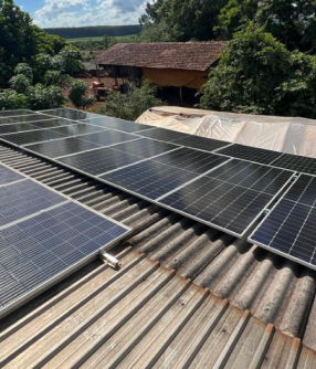 Painéis solares instalados em propriedade rural, com casa e mata ao fundo